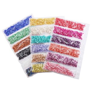 May include: Assortment of 14 small bags of colorful glitter, each bag containing a different color of glitter. The glitter is in a variety of shapes and sizes. The bags are arranged in a row, with the colors alternating.