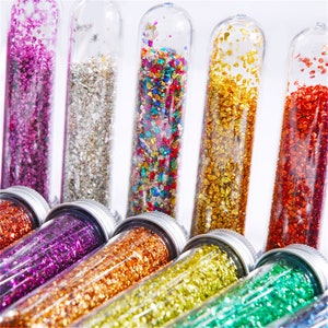 May include: Assortment of small glass tubes filled with colourful glitter. The tubes are clear and have silver caps. The glitter is in various colours, including red, gold, green, blue, purple, and silver.