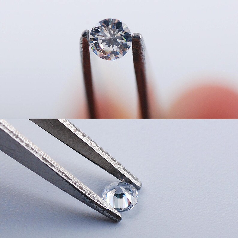 Pu&ograve; includere: Un diamante rotondo e trasparente tenuto da una pinzetta d'argento. Il diamante riflette la luce e ha un bagliore brillante.