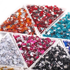 Può includere: Assortimento di piastrelle di vetro a specchio di forma quadrata in vari colori, tra cui argento, rosso, arancio, blu, nero e oro. Le piastrelle sono esposte in contenitori di forma triangolare.