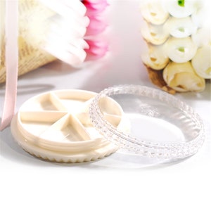 May include: A clear plastic lid with a textured edge sits on top of a white round container with seven compartments. The container has a scalloped edge.