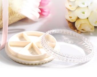May include: A clear plastic lid with a textured edge sits on top of a white round container with seven compartments. The container has a scalloped edge.