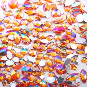 May include: Assortment of iridescent orange rhinestones in various shapes and sizes, including round, oval, square, and marquise.