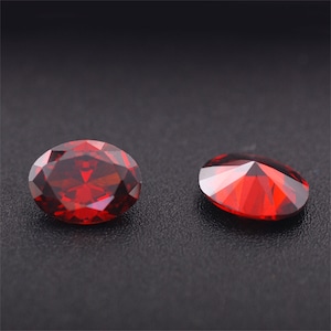 May include: Two red gemstone cabochons, one oval and one round, on a black background.