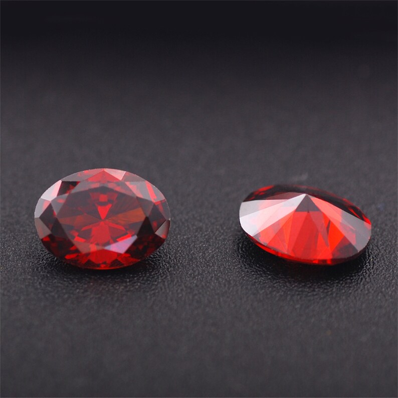 May include: Two red gemstone cabochons, one oval and one round, on a black background.