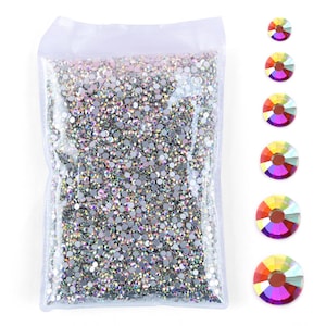 Puede incluir: Una bolsa de plástico transparente llena de una gran cantidad de pequeños diamantes de imitación redondos e iridiscentes que reflejan varios colores. A la derecha de la bolsa, seis diamantes individuales están dispuestos en línea vertical.