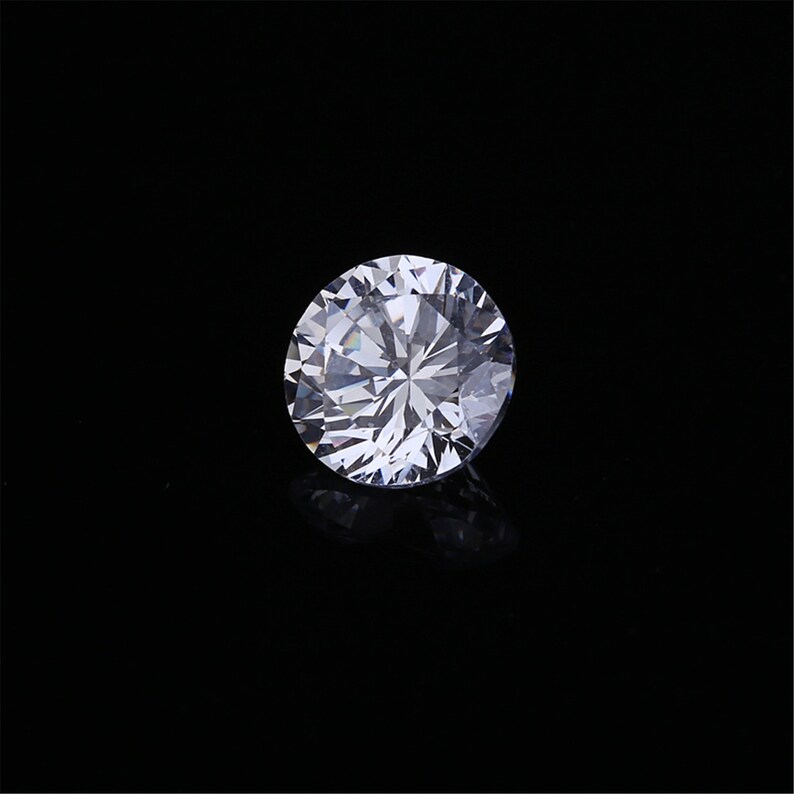 Pu&ograve; includere: Un diamante rotondo trasparente con molte sfaccettature, su uno sfondo nero.