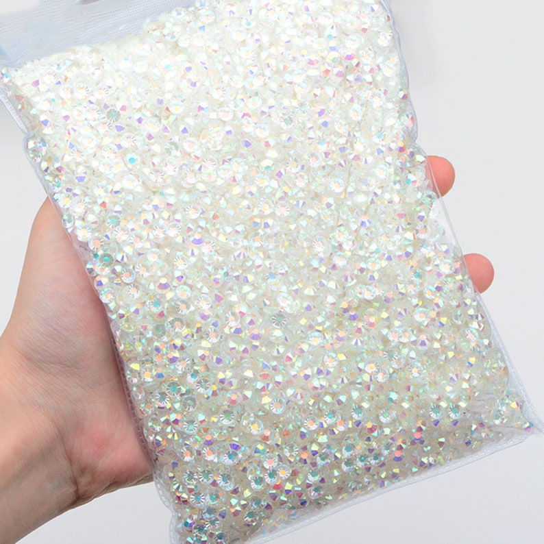 May include: A clear plastic bag filled with iridescent white rhinestones. The rhinestones are small and have a faceted, diamond-like appearance.