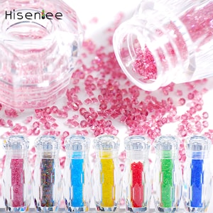 Könnte beinhalten: Sieben kleine Glasflaschen gefüllt mit buntem, schimmerndem Glitter. Die Flaschen sind klar und haben ein diamantförmiges Design. Der Glitter ist in verschiedenen Farben, darunter rosa, blau, grün, gelb und rot.