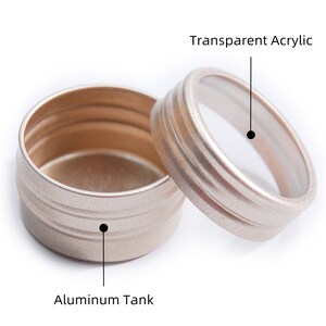 May include: A round, silver-coloured metal container with a transparent acrylic lid. The container has a ribbed design and the lid has a smooth surface.