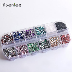 Puede incluir: Un organizador de plástico transparente lleno de pedrería redonda de varios colores. La pedrería es de color rojo, azul, morado, verde, plateado, rosa, marrón y negro. La marca "Hisentee" está impresa en negro.