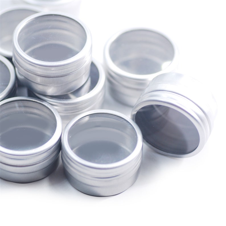 May include: A group of silver metal containers with clear plastic lids. The containers are stacked on top of each other and are all the same size.
