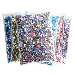 Può includere: Cinque sacchetti di strass quadrati iridescenti, ogni sacchetto riempito con un colore diverso di strass. I colori sono blu, verde, viola, arancione e rosso.