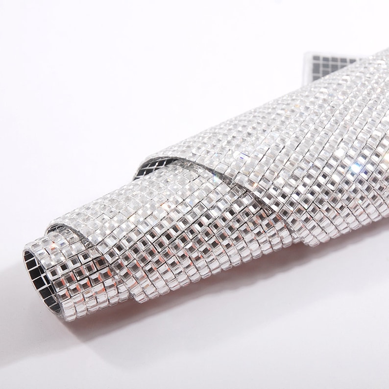 May include: A roll of silver adhesive backed rhinestones. The rhinestones are small and square shaped.