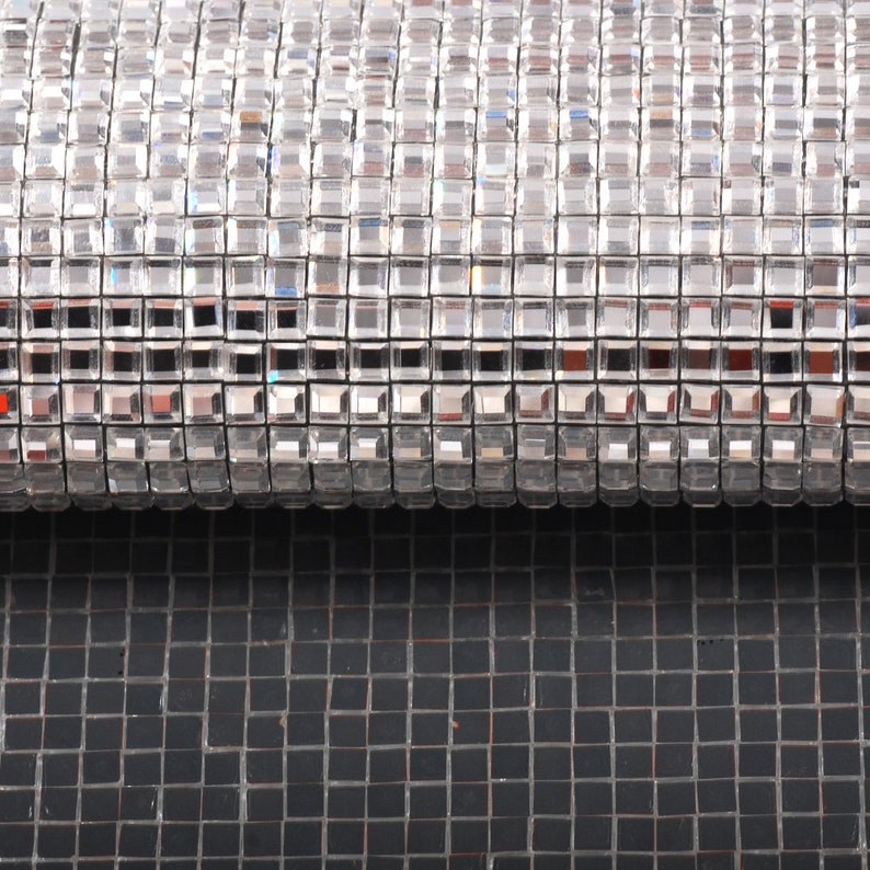 May include: A close-up of a silver, sparkly, square-shaped material. The material is rolled up and the top of the roll is visible. The material is on top of a black, square-shaped material.