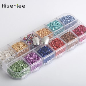 Puede incluir: Un recipiente de plástico transparente con 12 compartimentos llenos de escamas de purpurina de diferentes colores. El recipiente está lleno de varios colores, incluyendo plata, oro, rojo, verde, azul y morado. Se incluyen dos herramientas de arte para uñas plateadas.