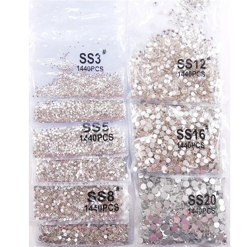 May include: Assortment of clear rhinestone crystals in various sizes, packaged in clear plastic bags. Each bag is labeled with the size of the rhinestones, such as SS3, SS5, SS8, SS12, SS16, and SS20, and the quantity, 1440PCS.