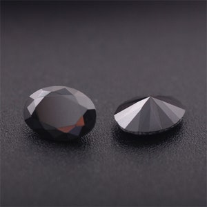 May include: Two black gemstones, one round and one oval, are displayed on a black surface. The round gemstone has a faceted design, while the oval gemstone has a smooth surface.
