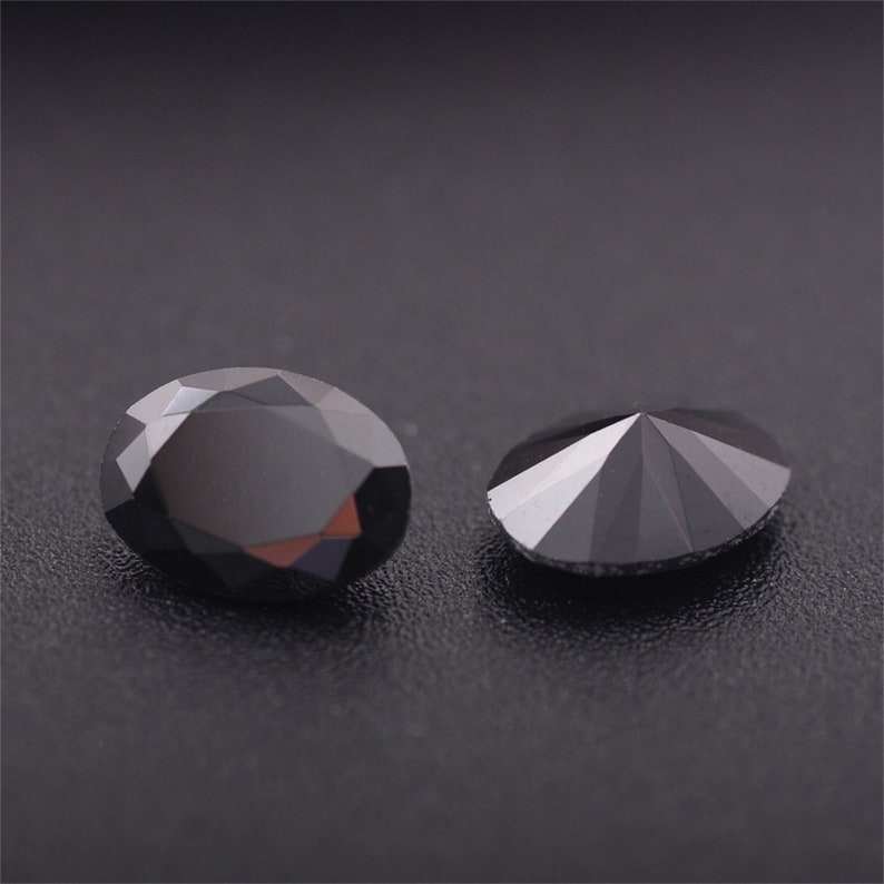 May include: Two black gemstones, one round and one oval, are displayed on a black surface. The round gemstone has a faceted design, while the oval gemstone has a smooth surface.
