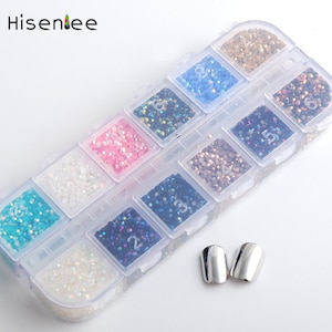 Puede incluir: Un recipiente de plástico transparente con 10 compartimentos llenos de purpurina de diferentes colores. Cada compartimento está etiquetado con un número. Dos puntas de uñas plateadas se encuentran en la esquina inferior derecha de la imagen.