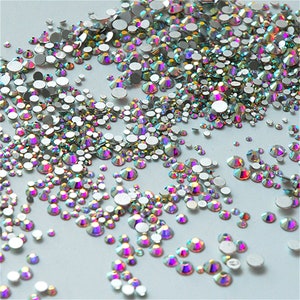 May include: A variety of iridescent rhinestones in different sizes, scattered on a white background.