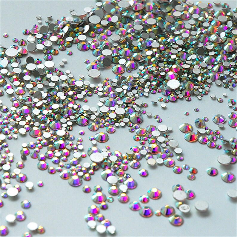 May include: A variety of iridescent rhinestones in different sizes, scattered on a white background.