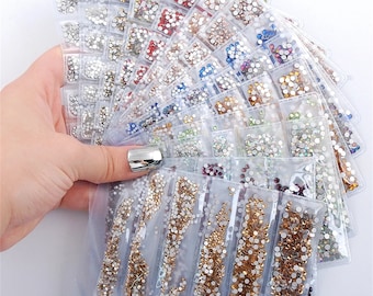 Pode incluir: Conjunto de strass transparentes, iridescentes e coloridos em sacos de plástico individuais. Os strass estão dispostos em forma de leque e estão prontos para projetos de artesanato.