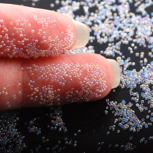 May include: Close-up of iridescent clear glass beads, scattered on a black surface. The beads are small and round, and they have a subtle shimmer.