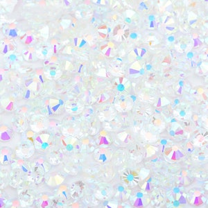 May include: A close-up image of iridescent white rhinestones. The rhinestones are scattered on a white background.