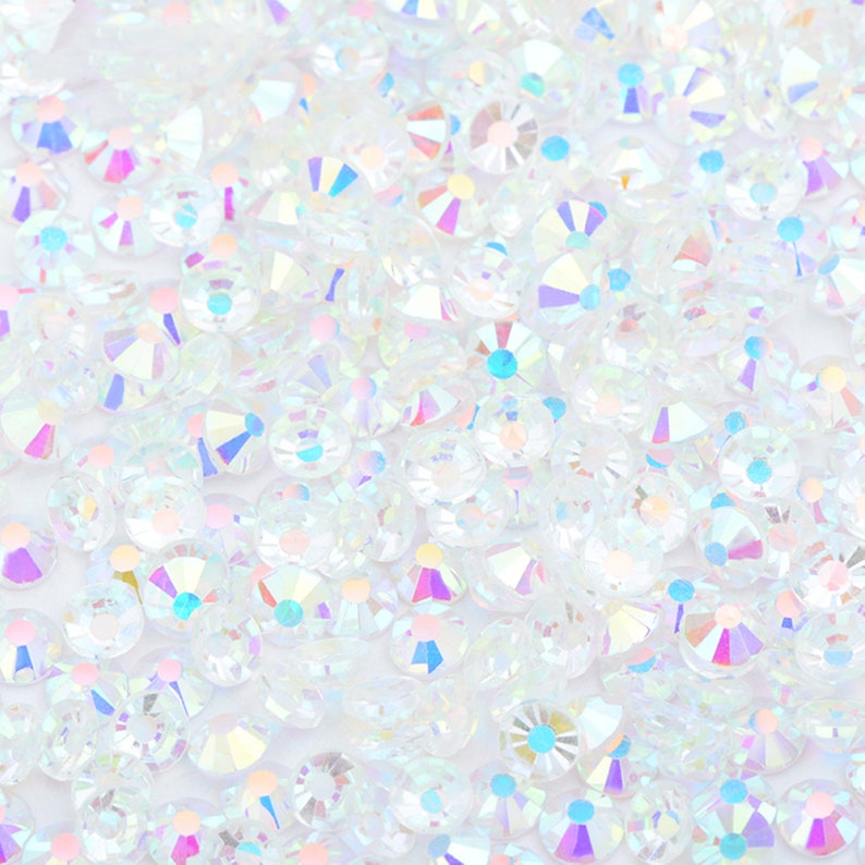 May include: A close-up image of iridescent white rhinestones. The rhinestones are scattered on a white background.