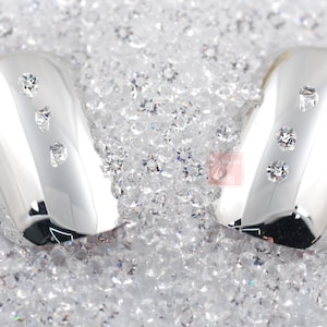 May include: Two silver oval-shaped nail tips with clear rhinestones set in a bed of sparkling clear crystals.