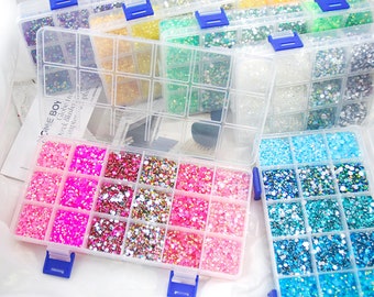 May include: A clear plastic storage box with multiple compartments filled with colorful rhinestones. The box has blue latches and is filled with various colors of rhinestones, including pink, blue, green, and clear.