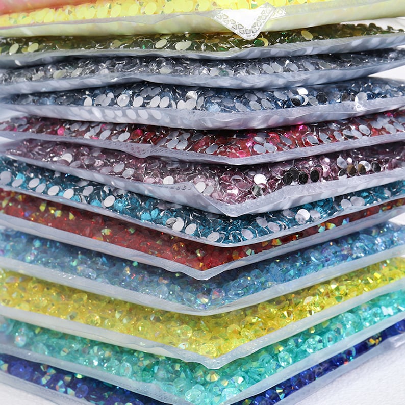 K&ouml;nnte beinhalten: Ein Stapel durchsichtiger Plastikt&uuml;ten, gef&uuml;llt mit verschiedenen Farben kleiner, runder Strasssteine. Die Strasssteine sind in Reihen angeordnet und durch die Plastikt&uuml;ten sichtbar.