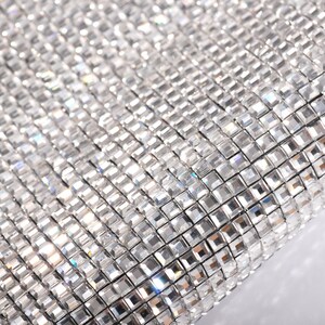 May include: Close-up of a silver sparkly fabric with a grid pattern of small square rhinestones.
