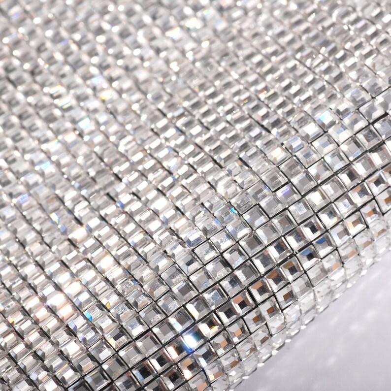 May include: Close-up of a silver sparkly fabric with a grid pattern of small square rhinestones.