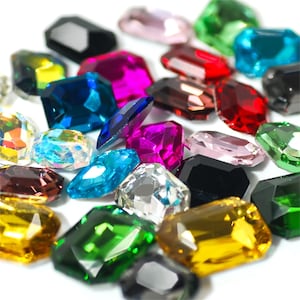 May include: Assortment of colorful faceted glass gems in various shapes and sizes. The gems are arranged on a white background.