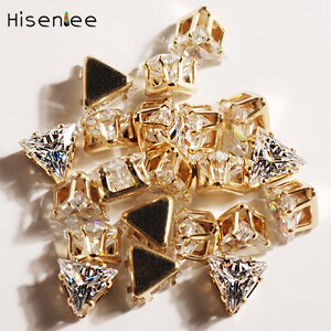 May include: A pile of gold-toned metal settings with clear crystal rhinestones. The settings are shaped like triangles and squares.