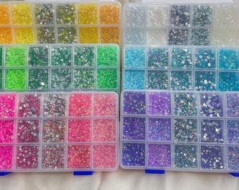May include: A clear plastic storage box with 36 compartments filled with various colors of rhinestones. The rhinestones are in different shades of yellow, green, blue, pink, and purple.
