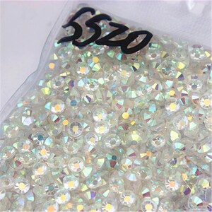May include: A close-up of a bag filled with clear iridescent rhinestones. The bag has a label that says "5520".