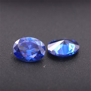 May include: Two oval-shaped, faceted, blue gemstones on a black surface.