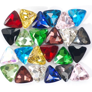 May include: Assortment of triangular shaped rhinestones in various colors, including red, blue, green, black, clear, and pink. The rhinestones are arranged in a random pattern on a white background.