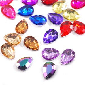 May include: Assortment of colourful teardrop-shaped glass rhinestones in various colours, including purple, blue, red, gold, and iridescent.
