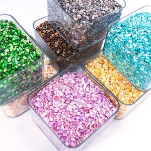 Puede incluir: Surtido de conchas marinas trituradas de colores en recipientes cuadrados transparentes. Las conchas son en tonos de verde, marrón, azul, amarillo y rosa.