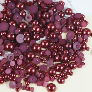 May include: A large assortment of burgundy and pink pearl beads and half-pearls. The beads are of various sizes and shapes, and some are flat.