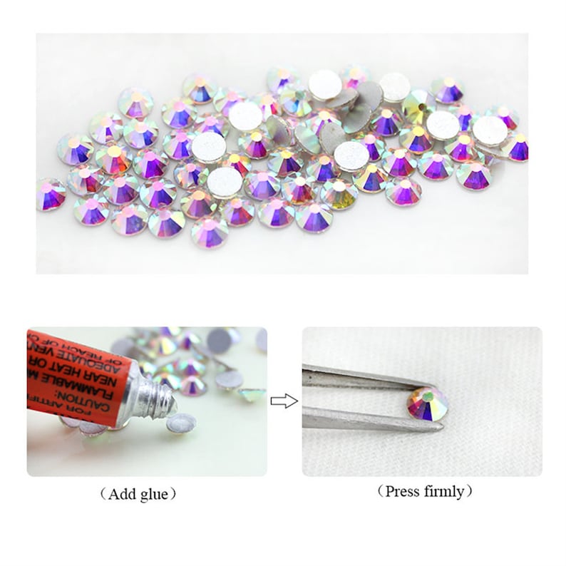 May include: A close-up of a pile of iridescent clear rhinestones with a white adhesive backing. The rhinestones are scattered on a white surface. A red tube of glue and tweezers are shown in the image to demonstrate how to apply the rhinestones.