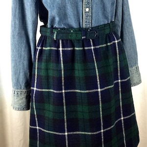 May include: A blue denim shirt with a plaid skirt. The skirt has a white belt.