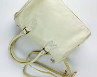 May include: A white leather handbag with a top handle and a long shoulder strap. The bag has a gold-toned zipper and hardware.