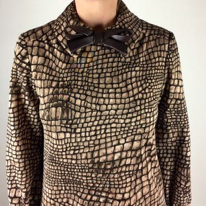 May include: A brown and beige long-sleeved blouse with a faux crocodile skin pattern. The blouse has a high collar and a brown bow tie.