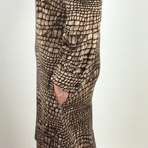 May include: A brown and beige dress with a crocodile print pattern. The dress has long sleeves and a collared neckline. The model is wearing black heeled shoes.