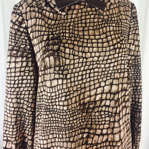 May include: A brown and beige long-sleeved dress with a crocodile print pattern. The dress has a brown faux leather bow at the collar.